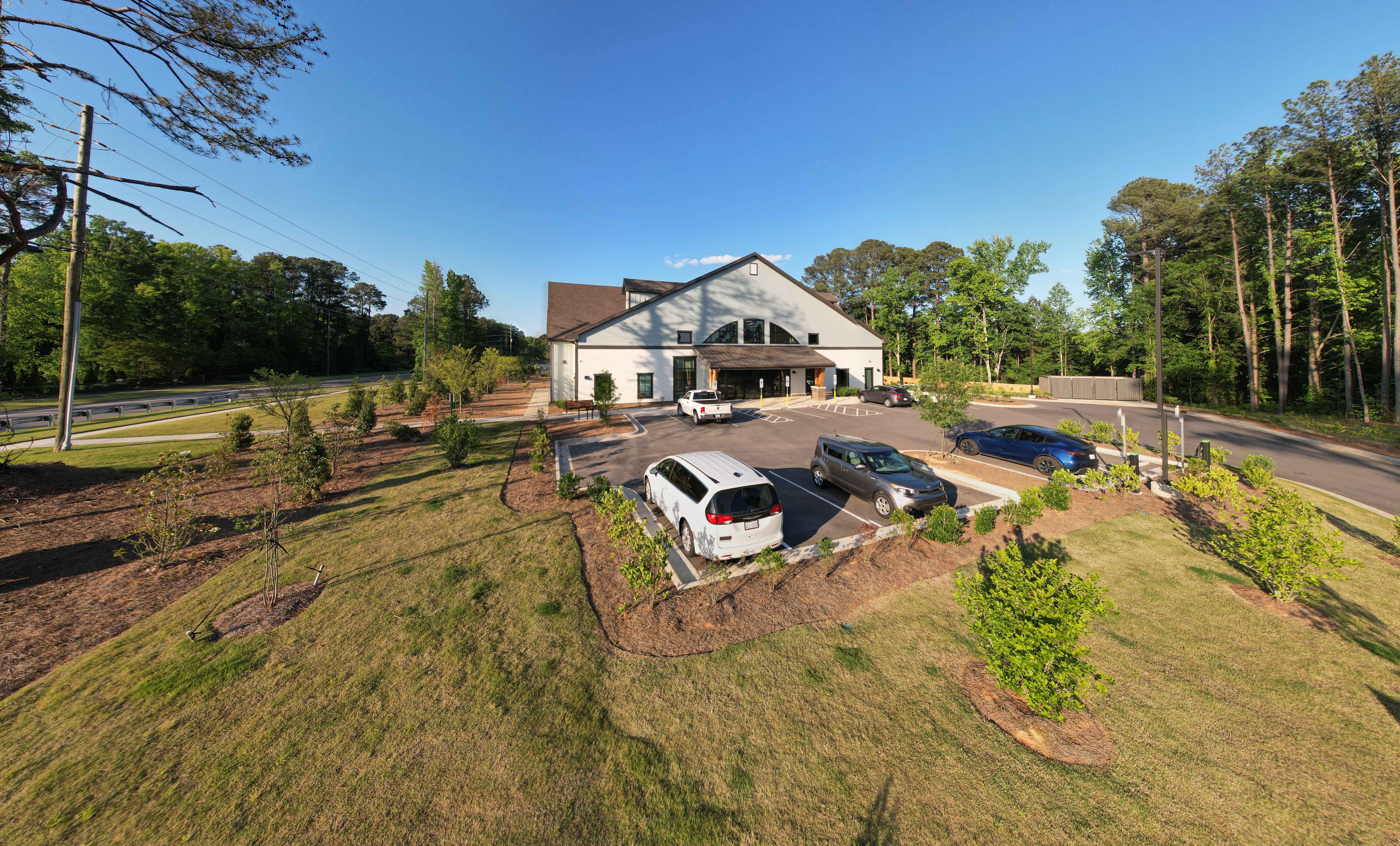 Wide side aerial view of a property with driveway, trees, and surrounding land